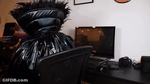A Person In A Black Costume Sits In Front Of A Computer Monitor GIF