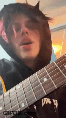 A Person In A Black Hoodie Is Playing A Guitar With The Word Dw On The Neck GIF