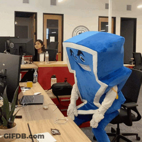 A Person In A Blue And White Costume Is Sitting At A Desk With A Laptop GIF