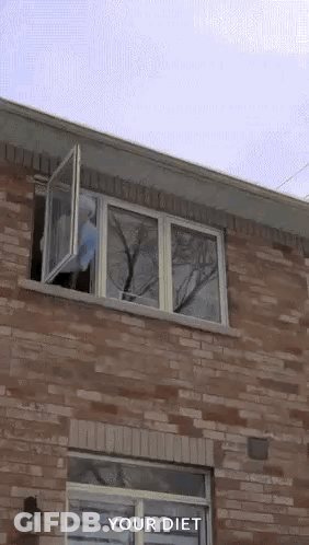 A Person In A Blue Hoodie Is Jumping Out Of A Window Of A Brick House . GIF