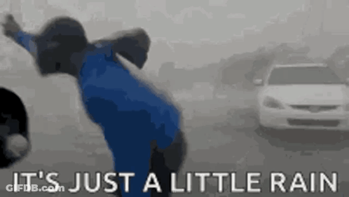A Person In A Blue Jacket Is Standing In The Rain With A Car In The Background . GIF