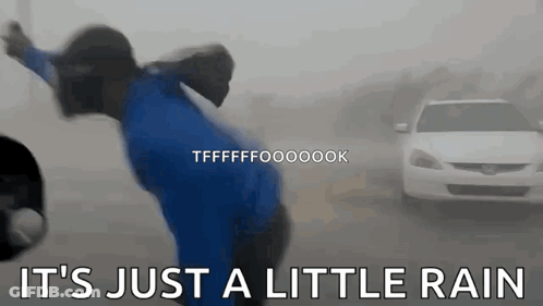 A Person In A Blue Shirt Is Standing In The Rain With A Car In The Background . GIF