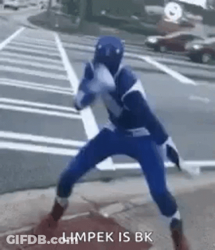 A Person In A Blue Superhero Costume Is Standing On A Sidewalk In A Parking Lot . GIF