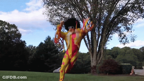 A Person In A Clown Costume Is Jumping In The Air In Front Of A Tree GIF