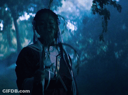 A Person In A Dark Forest Holding A Feather In Their Hand GIF