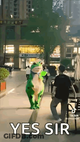 A Person In A Frog Costume Is Walking Down A Street . GIF