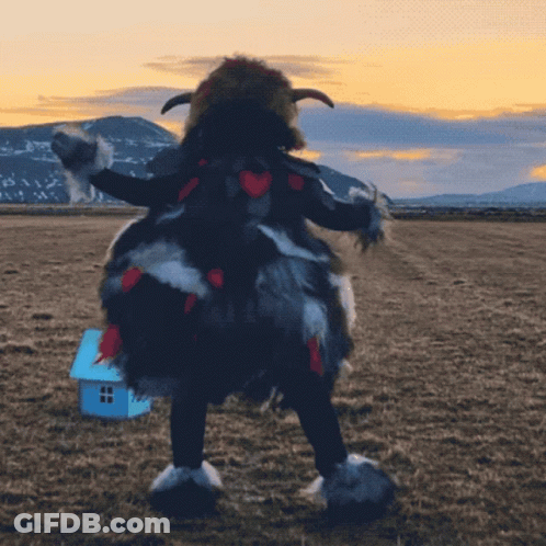 A Person In A Furry Costume Stands In A Field With A Small Blue House In The Background GIF