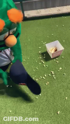 A Person In A Green Costume Is Kicking A Popcorn Bucket On The Grass . GIF