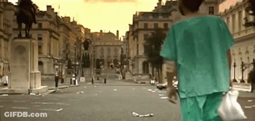 A Person In A Green Scrub Is Walking Down An Empty City Street . GIF