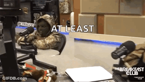 A Person In A Mask Is Sitting In Front Of A Microphone With The Words At Least Written On The Bottom GIF