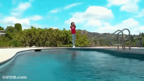 A Person In A Red Shirt Is Standing On The Edge Of A Swimming Pool . GIF