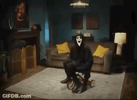 A Person In A Scary Mask Is Sitting On A Tricycle In A Living Room . GIF