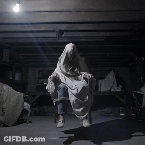A Person In A White Cloth Is Sitting In A Chair In A Dark Room GIF
