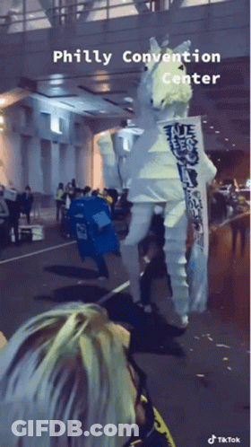 A Person In A White Seahorse Costume Is Walking Down The Street In Front Of The Philly Convention Center GIF