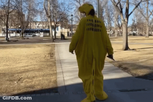 A Person In A Yellow Dinosaur Costume Is Walking Down The Sidewalk GIF