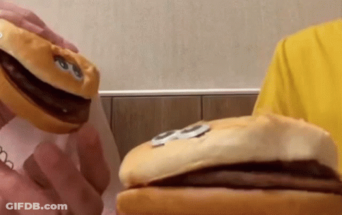 A Person In A Yellow Shirt Is Holding A Stuffed Hamburger With A Face On It GIF