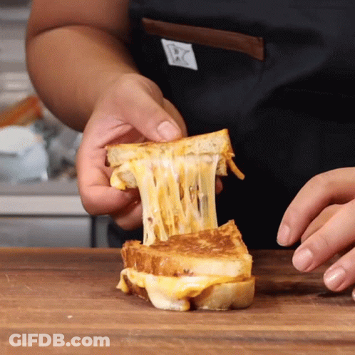 A Person In An Apron Is Holding A Grilled Cheese Sandwich With Cheese Coming Out Of It GIF