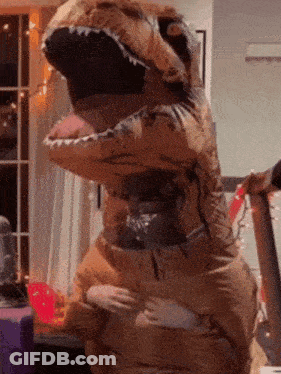 A Person In An Inflatable Dinosaur Costume Is Standing In A Room GIF