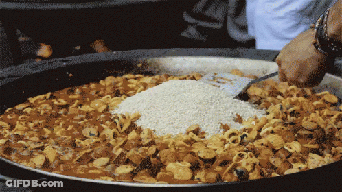 A Person Is Adding Rice To A Large Pot Of Food GIF