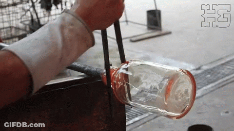 A Person Is Blowing A Glass Bottle With Tongs In A Factory GIF