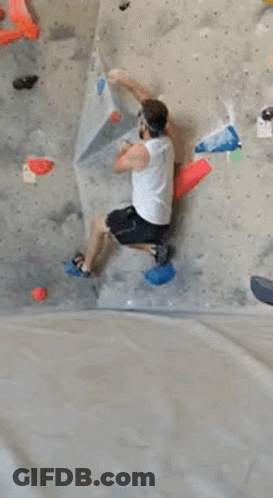 A Person Is Climbing A Climbing Wall In A Gym . GIF