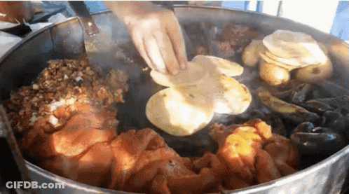 A Person Is Cooking A Bunch Of Food In A Large Pot GIF