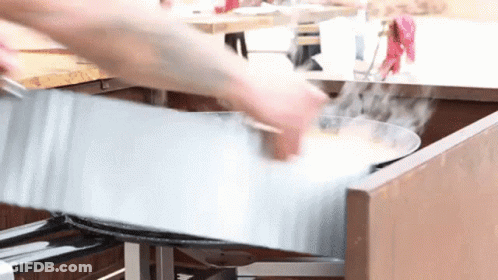 A Person Is Cooking Food In A Metal Pan In A Kitchen GIF