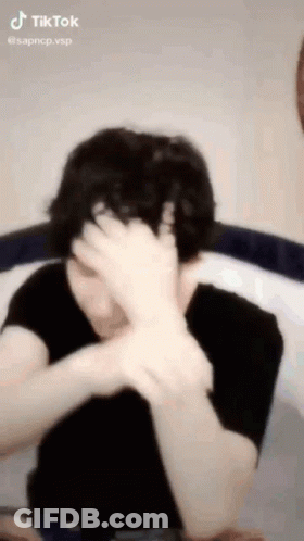 A Person Is Covering Their Face With Their Hand . GIF