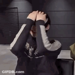 A Person Is Covering Their Face With Their Hands While Standing In Front Of A Wall . GIF