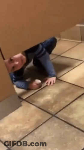 A Person Is Crawling Under A Wall In A Public Restroom Holding A Cup . GIF