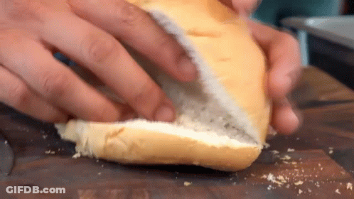 A Person Is Cutting A Bun In Half On A Cutting Board . GIF