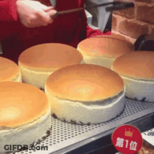 A Person Is Cutting A Cheesecake With A Knife In A Bakery . GIF