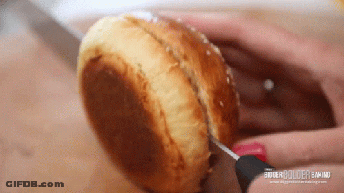 A Person Is Cutting A Hamburger Bun With A Knife And It Says Bigger Bolder Baking On The Bottom Right GIF