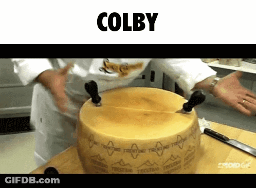 A Person Is Cutting A Large Piece Of Cheese With The Name Colby Written Above Them GIF