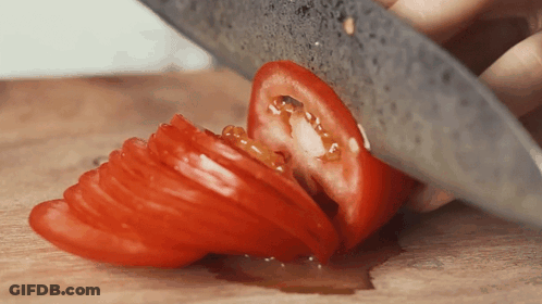 A Person Is Cutting A Tomato In Half On A Cutting Board GIF