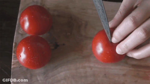 A Person Is Cutting A Tomato With A Knife On A Cutting Board GIF