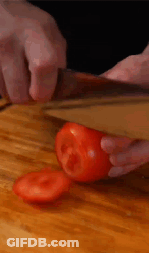 A Person Is Cutting A Tomato With A Knife On A Wooden Cutting Board GIF