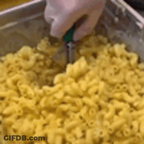 A Person Is Cutting Macaroni And Cheese With A Knife In A Pan . GIF