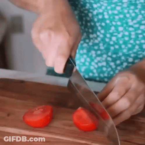 A Person Is Cutting Two Tomatoes On A Wooden Cutting Board . GIF