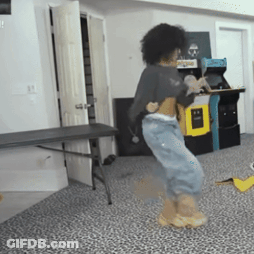 A Person Is Dancing In A Room With An Arcade Machine In The Background And A Table In The Foreground GIF