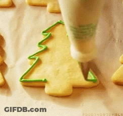 A Person Is Decorating A Cookie In The Shape Of A Christmas Tree With Green Frosting GIF