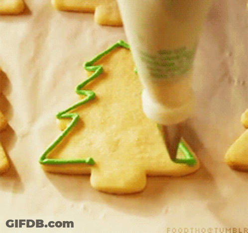 A Person Is Decorating A Cookie In The Shape Of A Christmas Tree With Green Frosting GIF