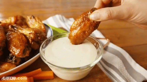A Person Is Dipping A Chicken Wing Into A Bowl Of Ranch Dressing GIF