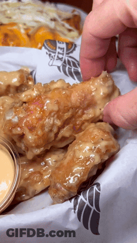 A Person Is Dipping A Chicken Wing Into A Sauce That Says Wings GIF