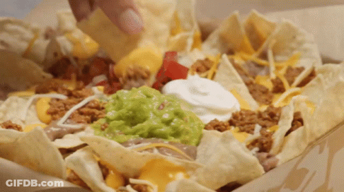 A Person Is Dipping A Chip Into A Bowl Of Nachos With Guacamole And Sour Cream GIF