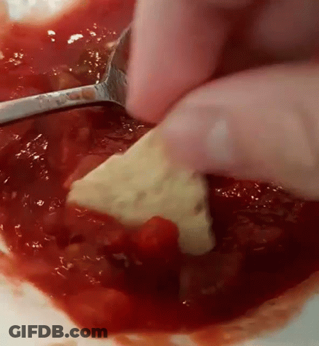 A Person Is Dipping A Cracker In A Bowl Of Tomato Sauce . GIF