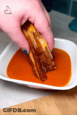 A Person Is Dipping A Grilled Cheese Sandwich In A Bowl Of Sauce GIF