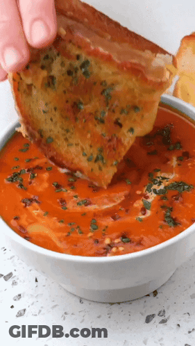 A Person Is Dipping A Piece Of Grilled Cheese Into A Bowl Of Soup GIF