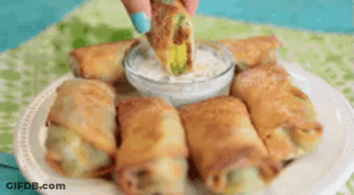 A Person Is Dipping An Egg Roll In Ranch Dressing On A Plate Of Food . GIF