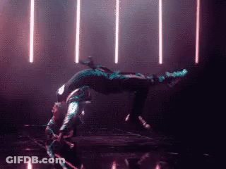 A Person Is Doing A Handstand In A Dark Room With Lights Behind Them GIF